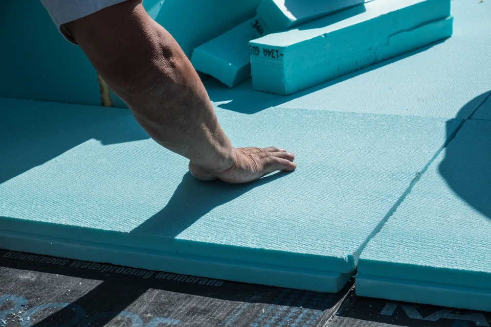Ouvrier posant des panneaux d'isolation thermique bleu-vert sur une surface extérieure, main droite appuyée pour ajuster les matériaux