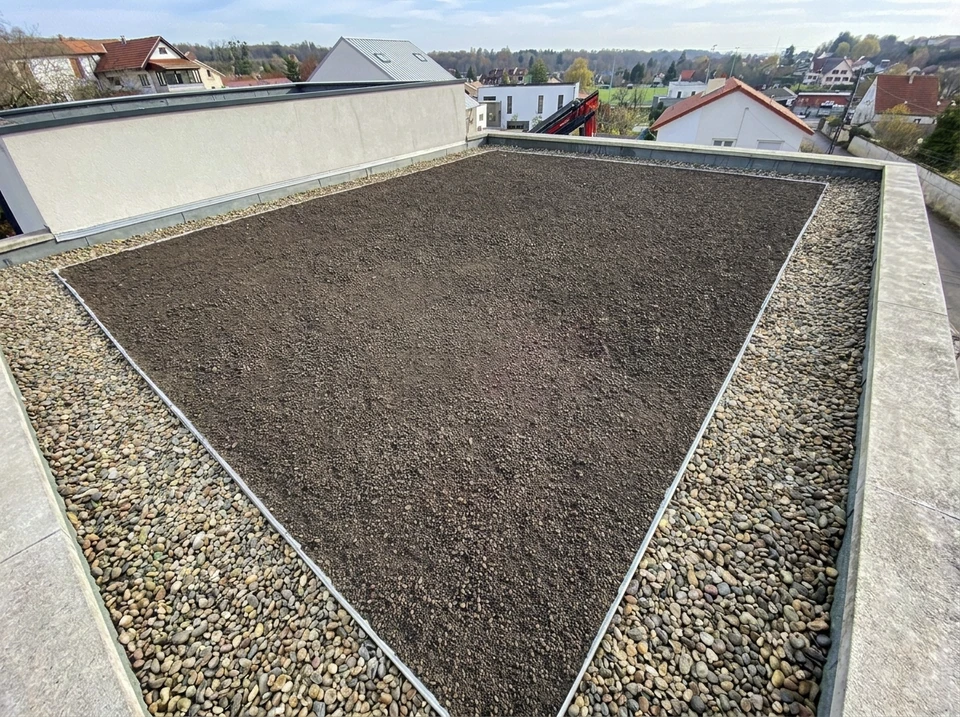 Ouvrier en combinaison bleue et jaune applique un revêtement d'étanchéité bleu sur surface béton extérieure avec rouleau à manche télescopique