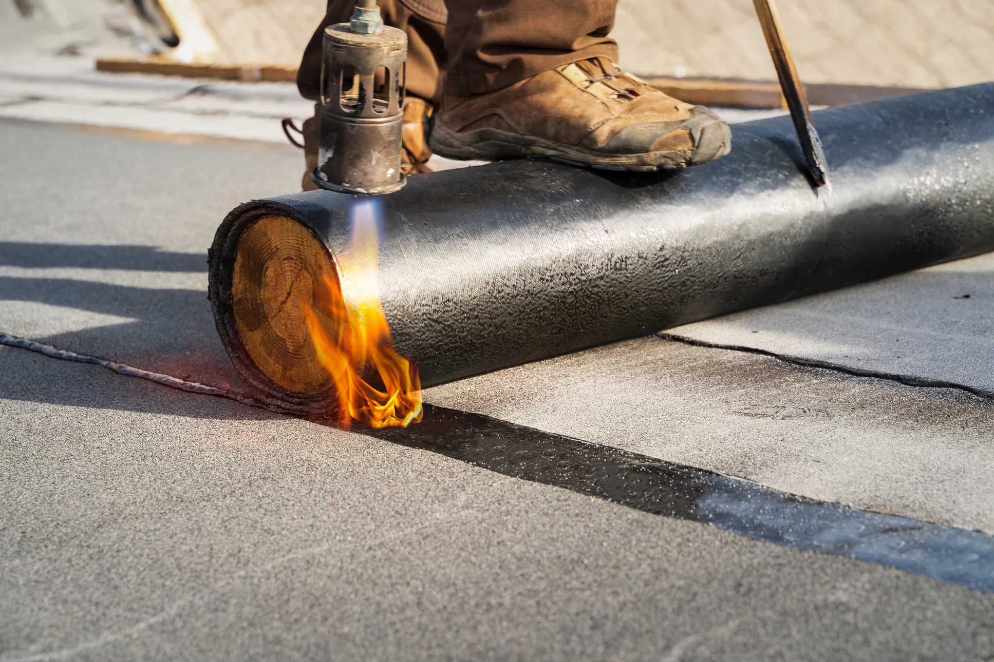 Ouvrier en tenue de travail appliquant un revêtement d'étanchéité sur une terrasse extérieure à l'aide d'un chalumeau à gaz