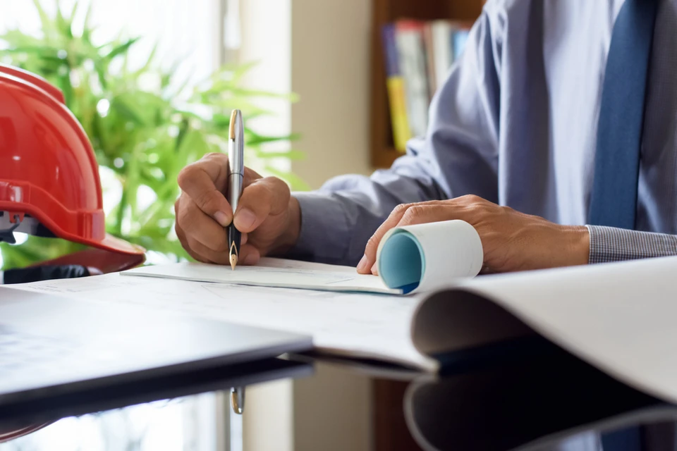 Scène de bureau d'architecture ou d'ingénierie avec casque de chantier jaune, plans roulés et tampon encreur sur table blanche